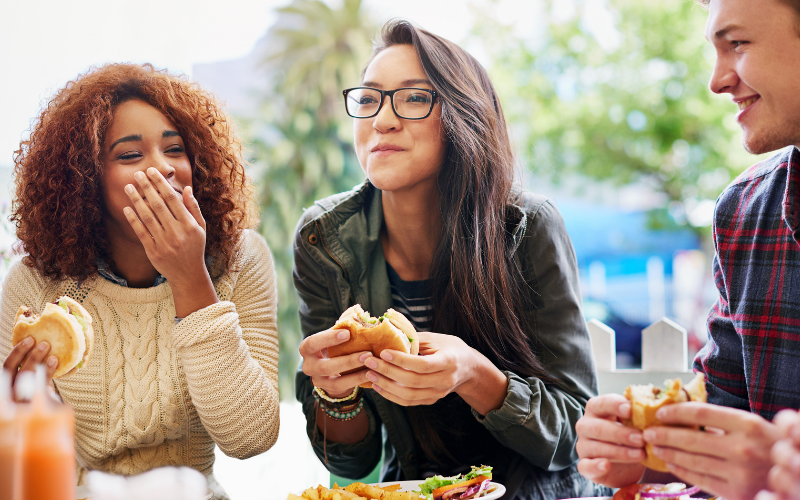 Three people eating burgers outside